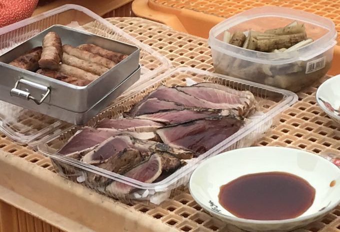 畑にコンテナを広げ、カツオのタタキを食べる